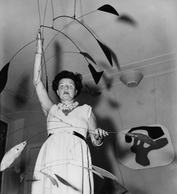 Peggy Guggenheim with Alexander Calder’s “Arc of Petals” mobile, and Jean Arp’s “Overturned Blue Shoe” on the wall behind her.